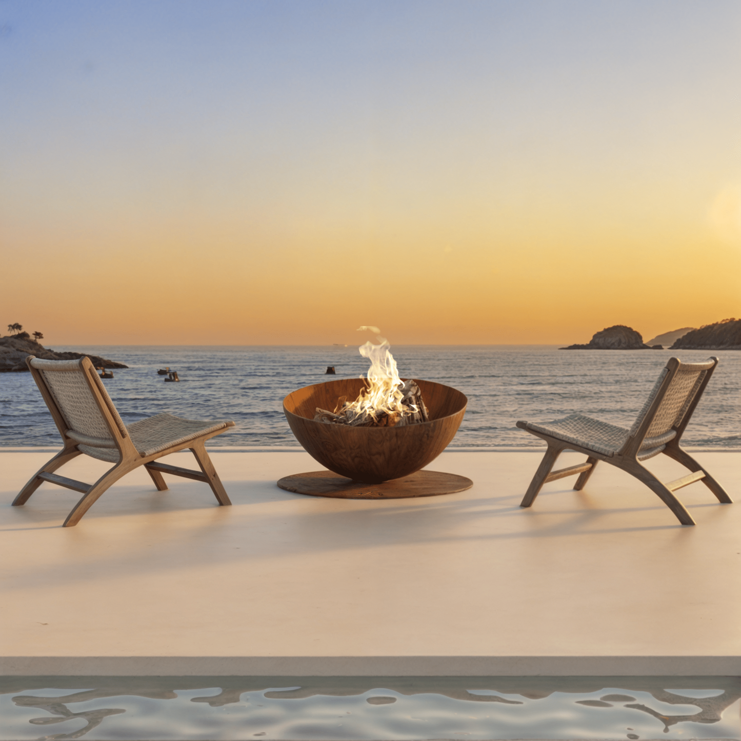 Two lounge chairs by a fire pit on a patio with a scenic ocean view at sunset.