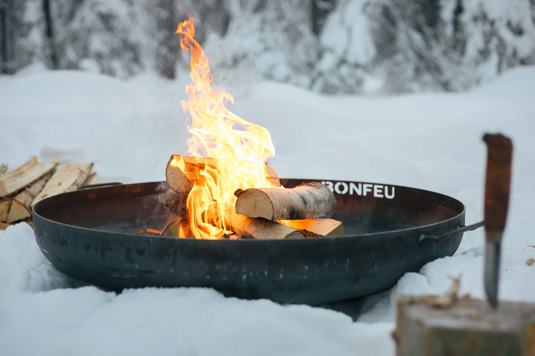 A BonFeu BonBowl Plus Corten steel fire pit lit on a snow-dusted patio — built to live outside through every British season