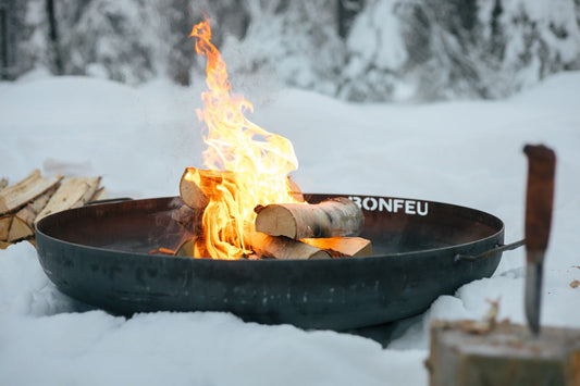 A BonFeu BonBowl Plus Corten steel fire pit lit on a snow-dusted patio — built to live outside through every British season