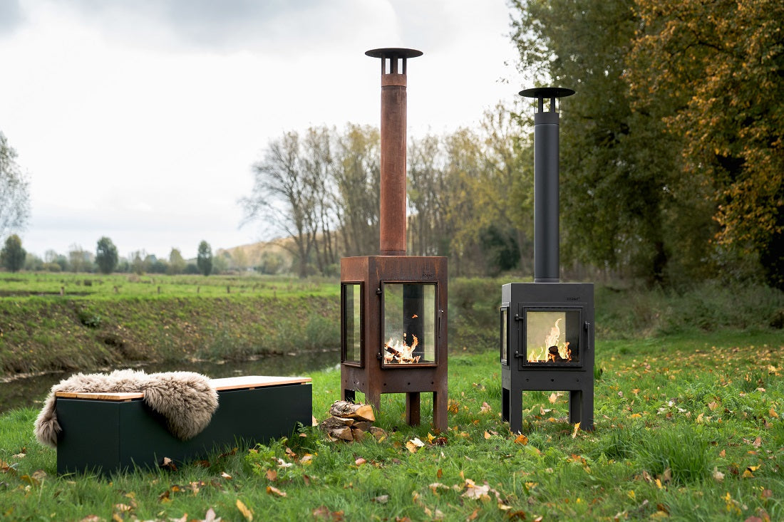 Two upright Adezz Digna outdoor fireplaces, Corten and black coated steel, lit in an autumn meadow setting