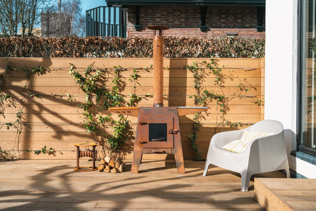 Adezz Damm Corten Steel outdoor fireplace on a sunlit wooden terrace with climbing vines and modern white chair