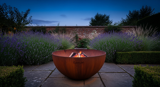 A russet corten steel fire pit bowl with glowing amber embers in an English cottage garden at dusk