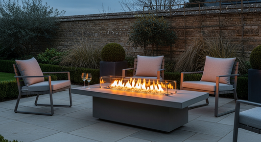 Subject: a considered British patio garden at dusk in late spring. A contemporary rectangular gas fire pit table sits at centre frame on smo