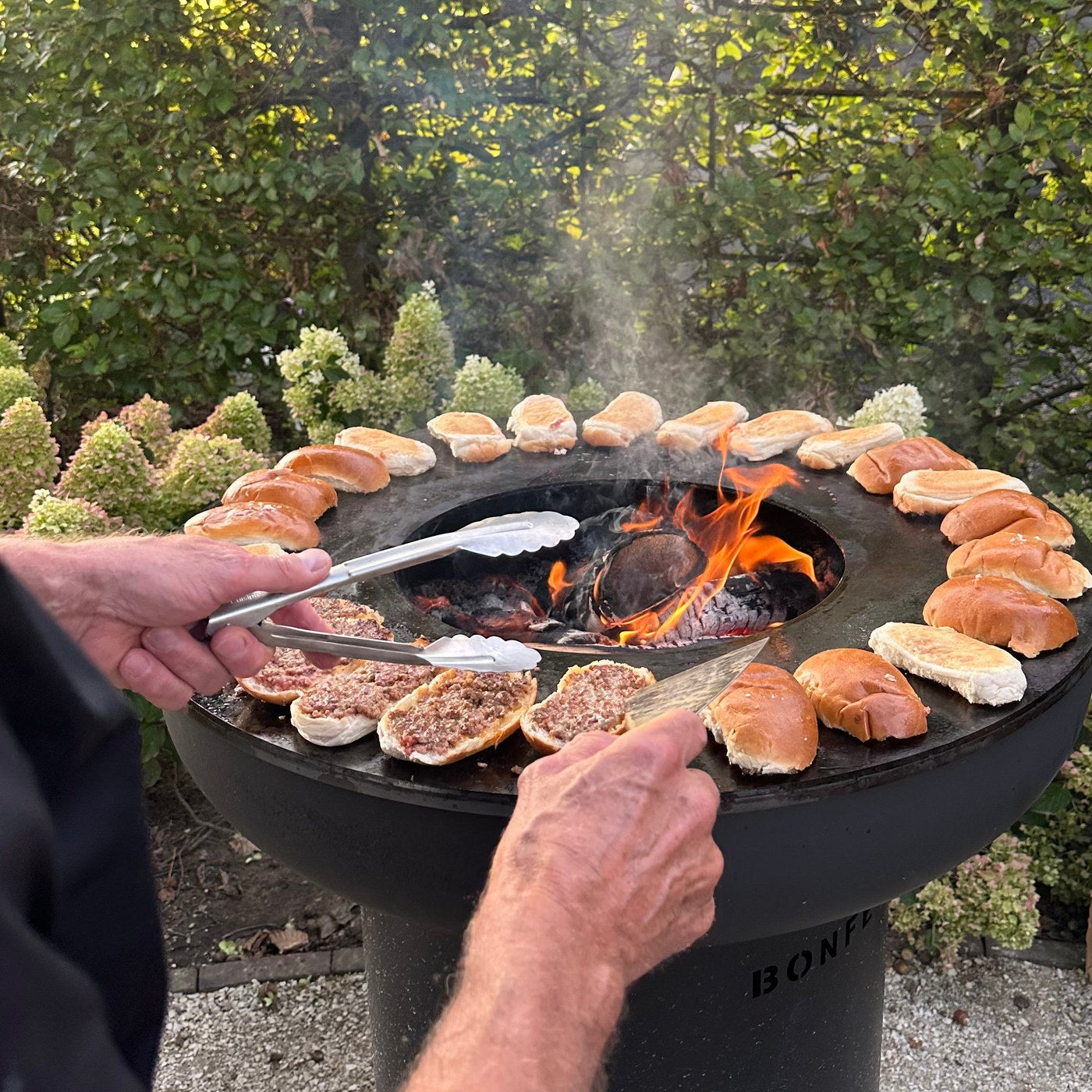 Cooking burgers and buns on the plancha ring of a BonFeu BonBiza outdoor fire pit